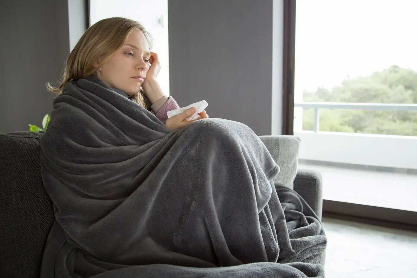 A bored, sick woman with one hand on her head, holding a napkin in the other.