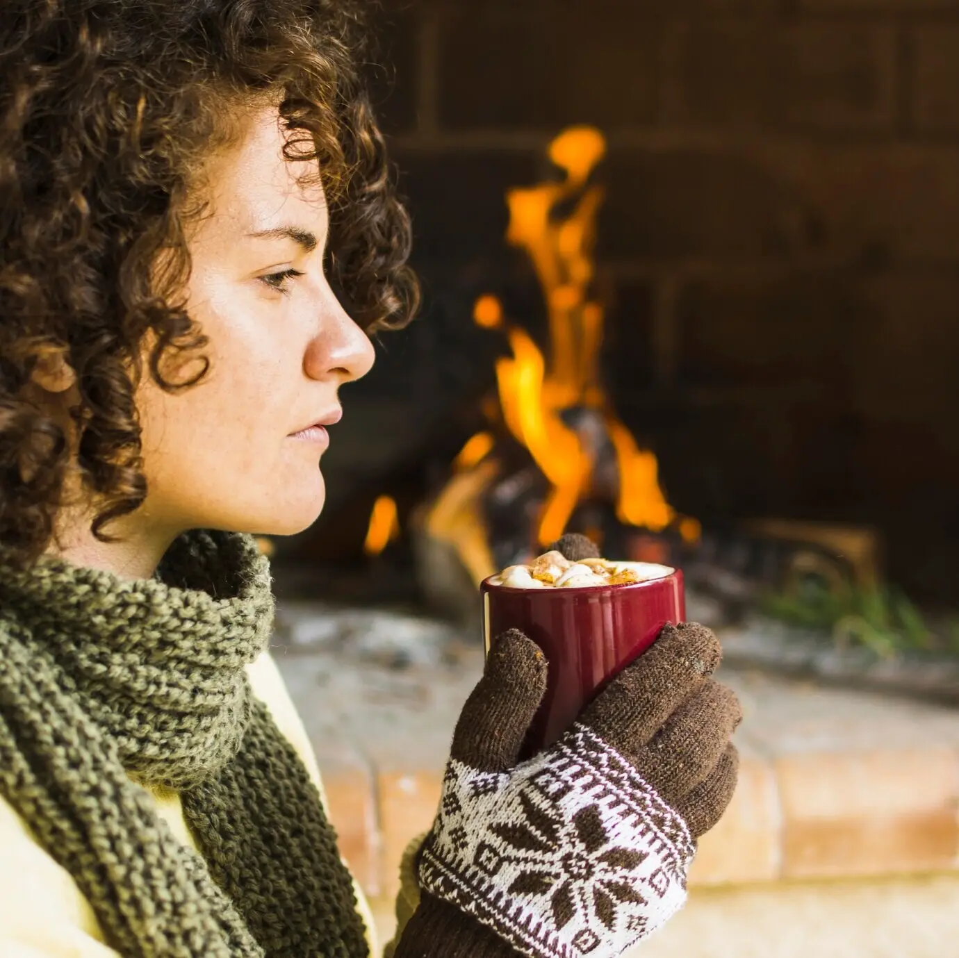 Woman enjoying a hot drink near a fireplace.